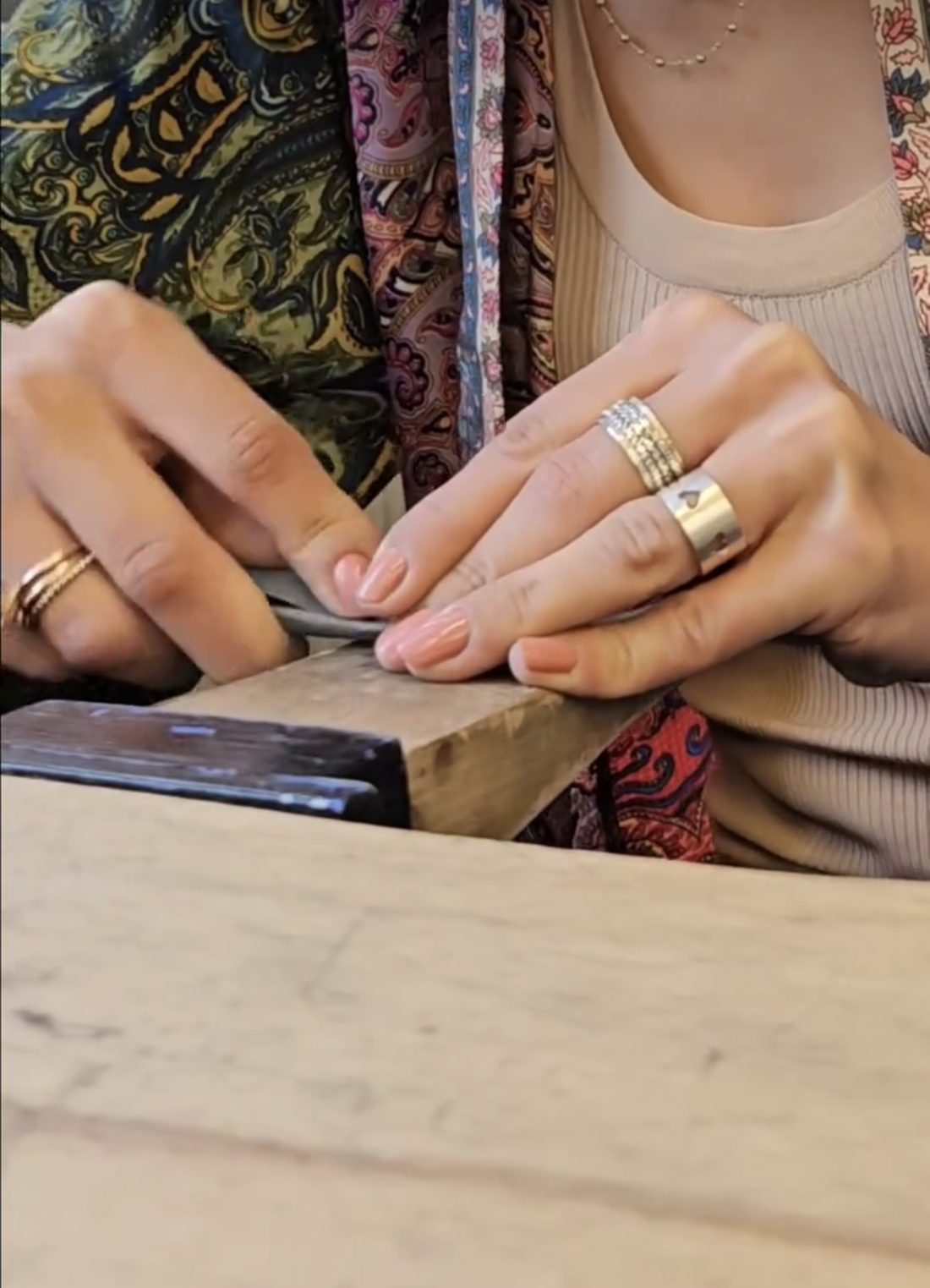 Handen met ringen die een stuk metaal vijlen aan de werkbank